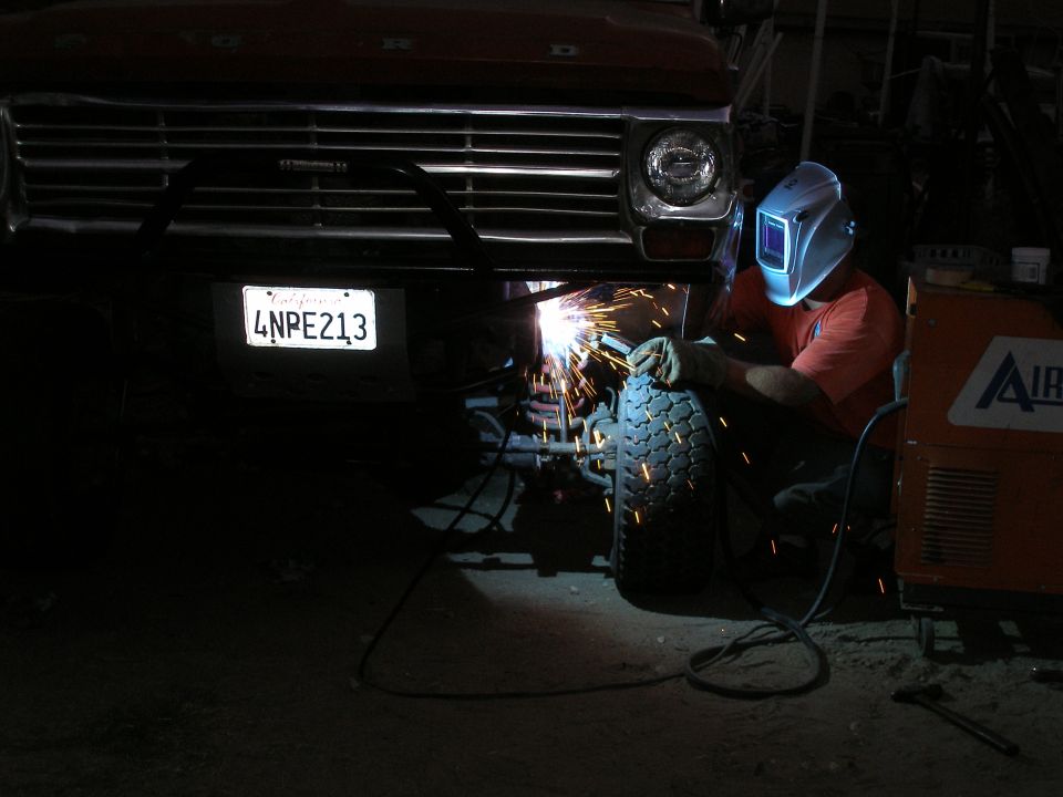 Welder working on the front bumper of a red truck, license plate 4NPE213 visible