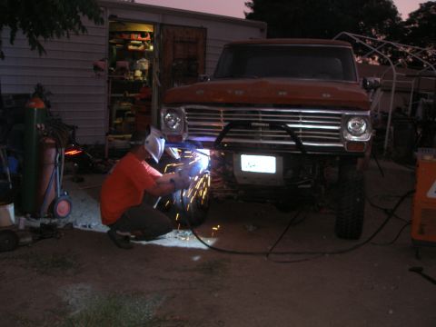 1969 Ford F-250 - A person welds a custom bumper onto an orange Ford truck in front of a garage.