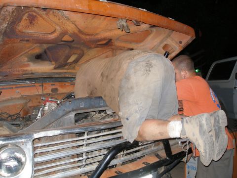 1969 Ford F-250 - Mechanics work on the engine bay of an orange truck, with another vehicle in the background.