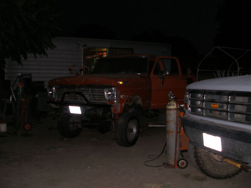 Orange pickup truck with its door open, parked next to a white truck. Looks like it's in a yard at night