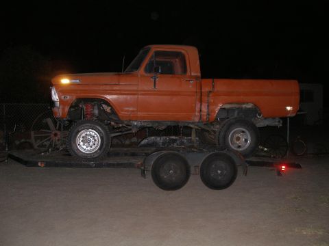 1969 Ford F-250 - Side view of an orange 1967 Ford F-100 pickup truck with a lifted suspension on a trailer.