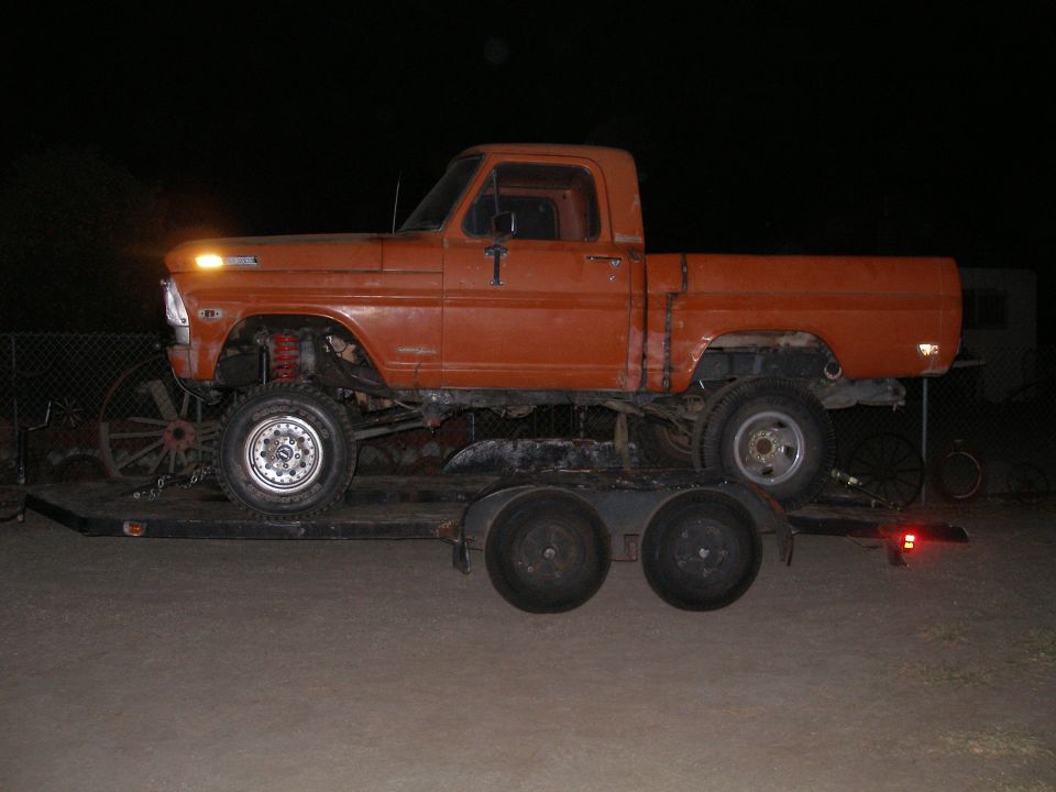 Orange 1967 Ford F-100 pickup truck with lifted suspension on a car trailer at night