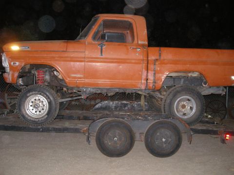1969 Ford F-250 - A lifted orange pickup truck is being transported on a trailer at night.