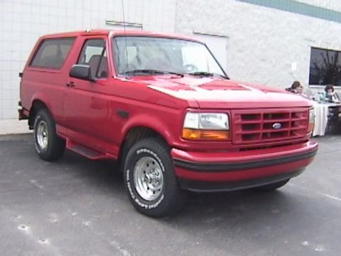 1995 Ford Bronco - This red Ford Bronco is parked in front of a building with people sitting at tables in the background.
