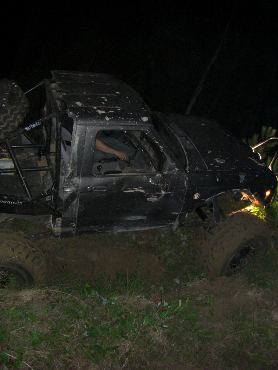 Black off-road SUV with roll cage stuck in mud at night