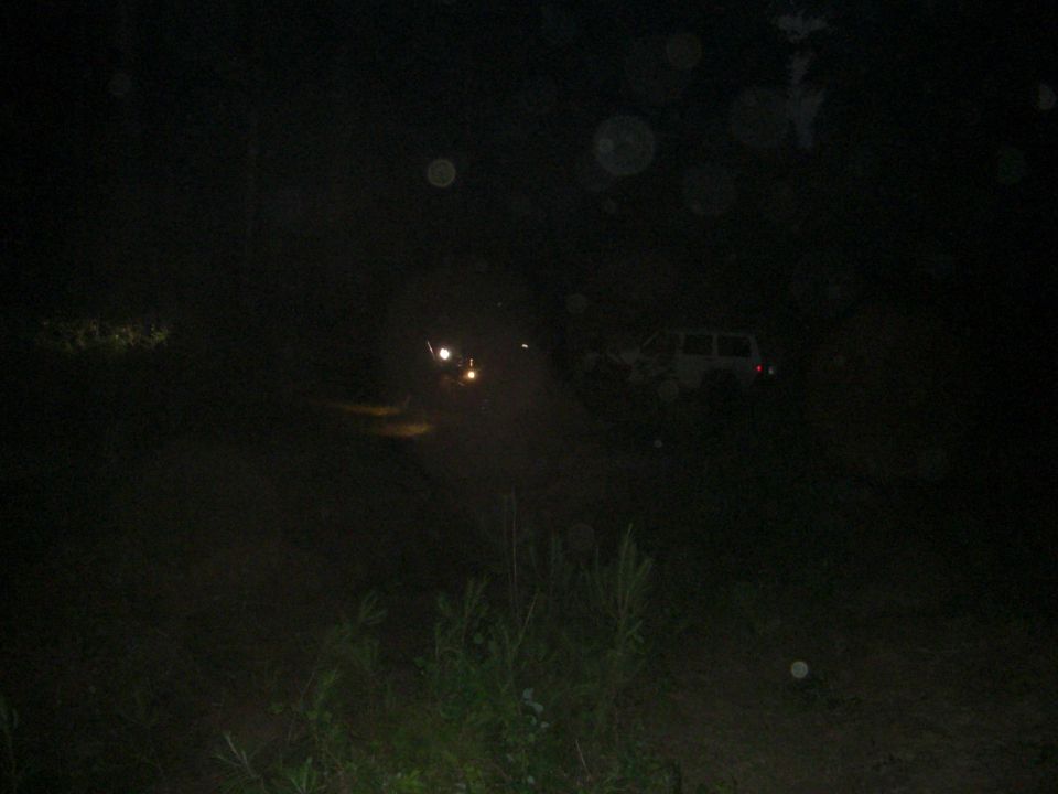 Two SUVs are visible on a dirt road at night, with headlights on
