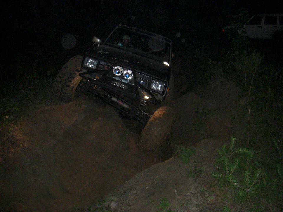 Black off-road SUV with aftermarket bumper and lights navigating a muddy ditch at night