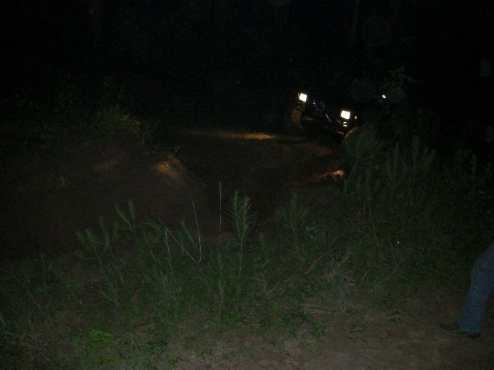 Off-road vehicle with headlights on, driving on a dirt path at night