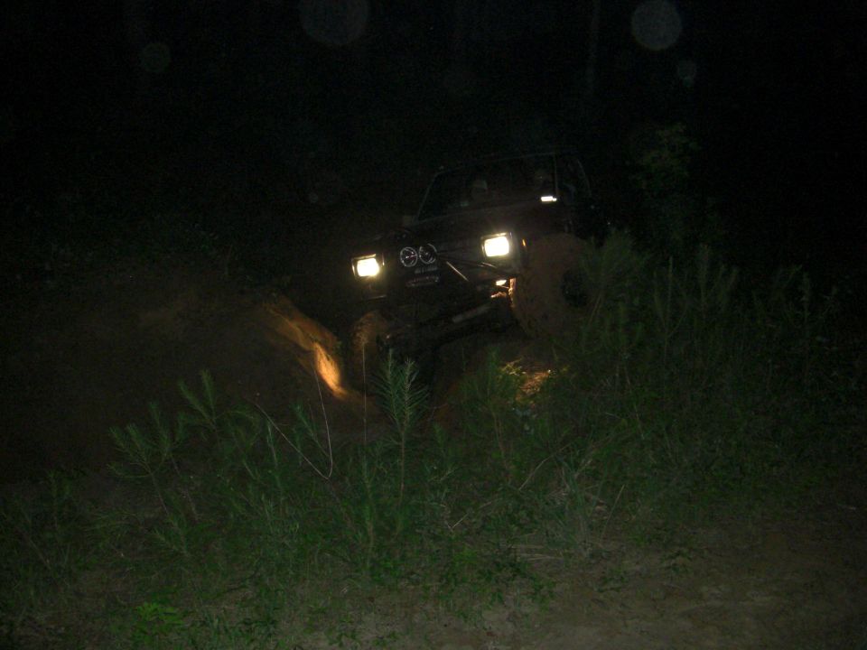 Off-road SUV driving through mud at night with headlights on