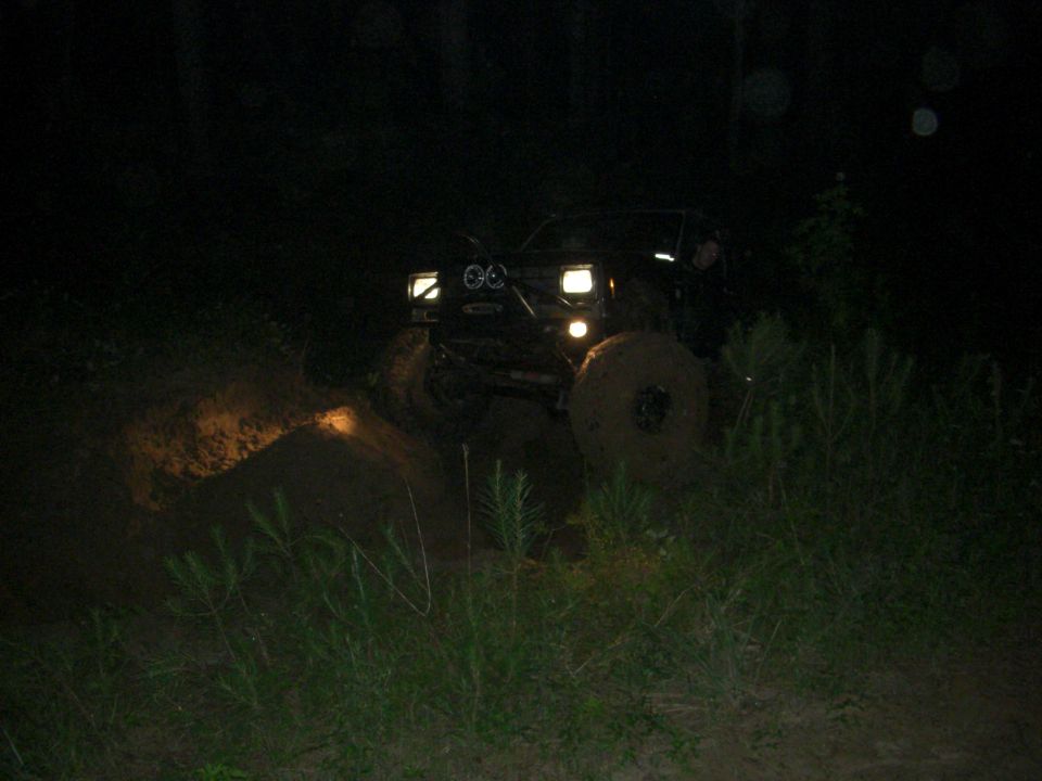 Black off-road vehicle with large tires driving through mud at night