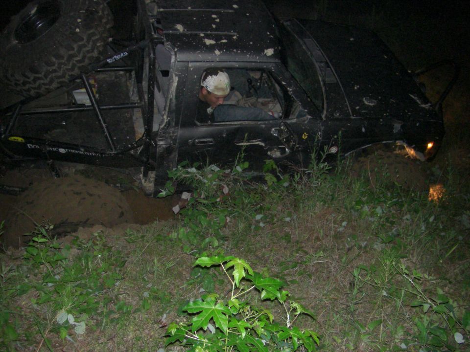 Black off-road truck with a spare tire on top, stuck in mud with a person inside