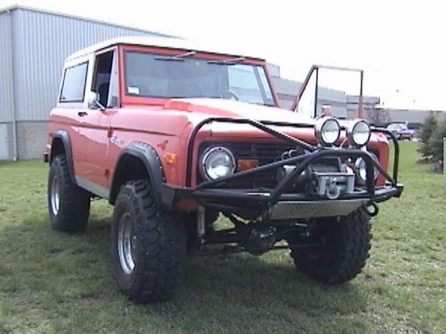 Red Ford Bronco with a winch and extra lights on the front bumper, parked on grass