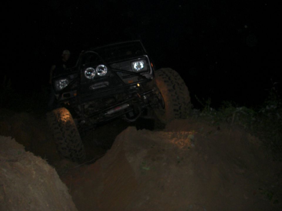 Black off-road vehicle with dual headlights and large tires climbing a dirt hill at night