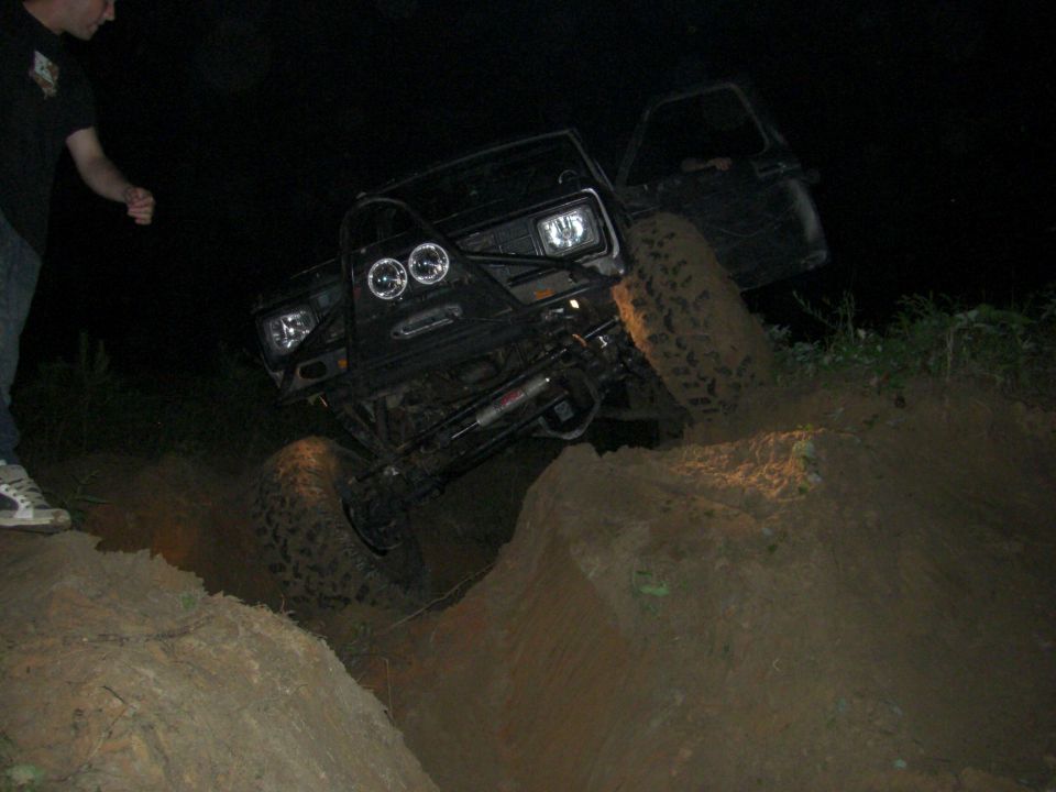Black off-road SUV with aftermarket bumper and lights climbing a dirt hill at night