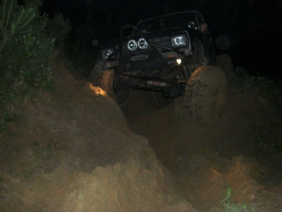 Off-road vehicle with auxiliary lights climbing a muddy hill at night