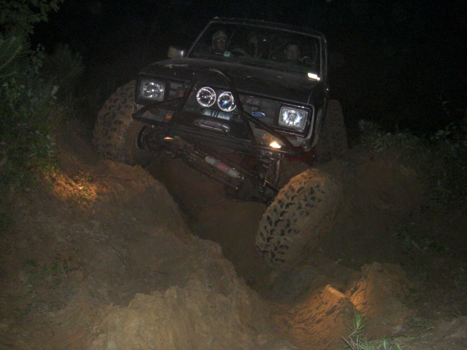 Black 1984 Ford Bronco II climbing a steep, muddy incline at night