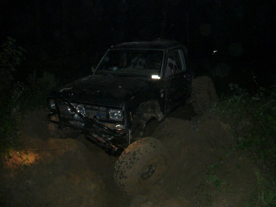 Black SUV stuck in mud at night, with large tires and a modified bumper