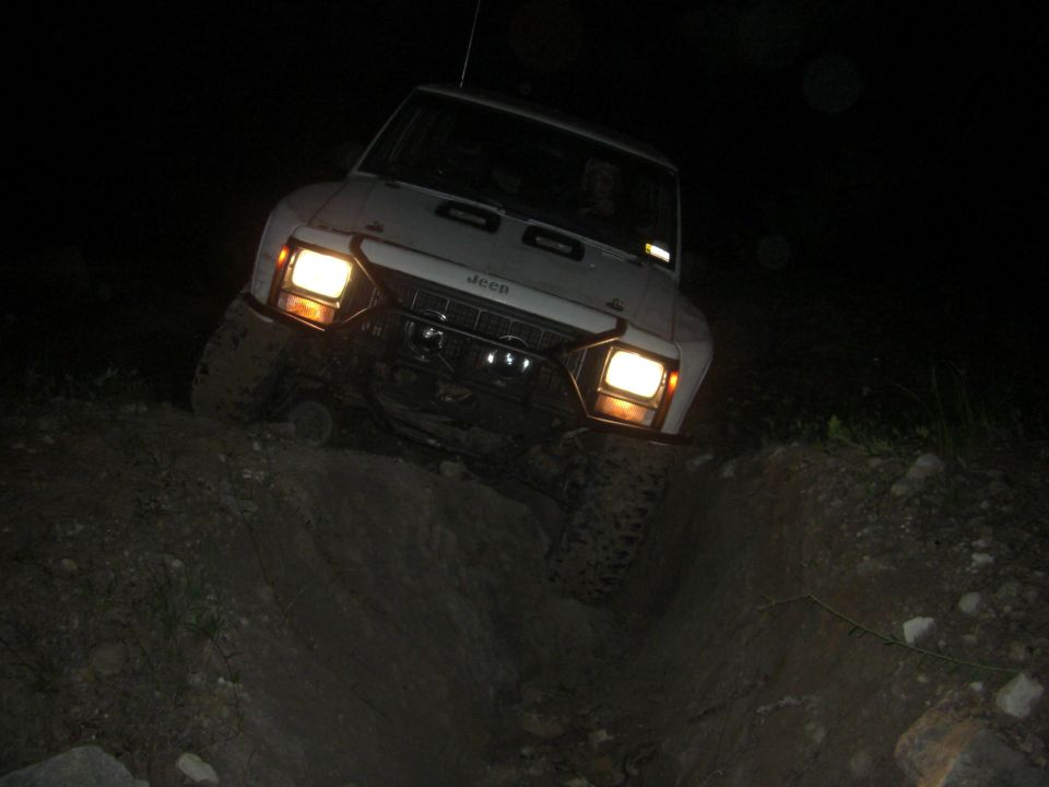 White Jeep Cherokee XJ driving off-road at night, headlights on