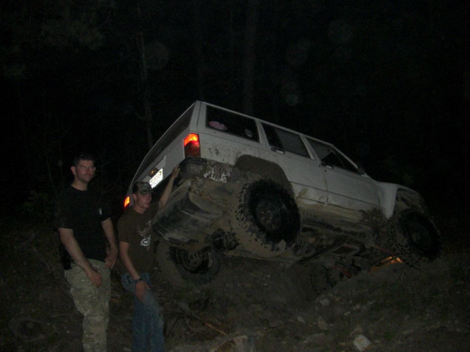 White SUV tilted on muddy terrain at night, two men standing nearby