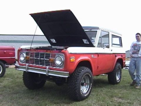 1995 Ford Bronco - This red and white Ford Bronco, likely from the 1970s, is displayed with its hood open, revealing the engine bay.