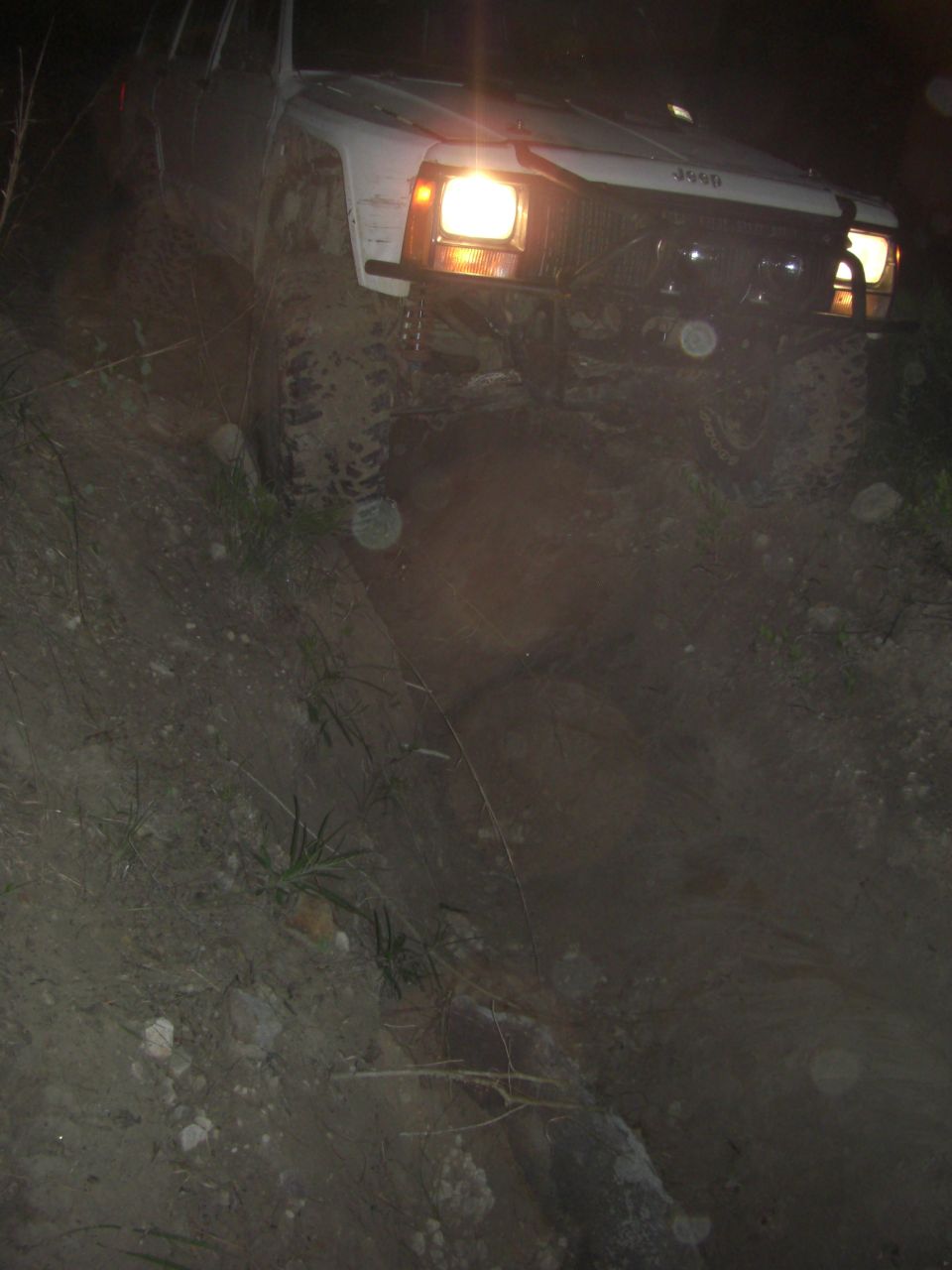 White Jeep Cherokee XJ on a dirt incline at night, headlights on