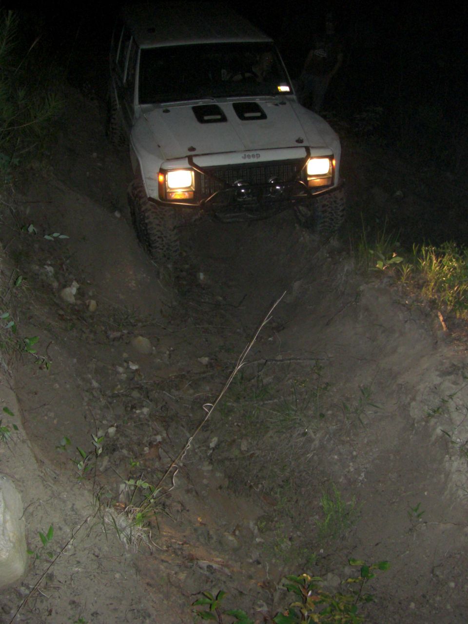 White Jeep Cherokee XJ driving on a dirt path at night, headlights on