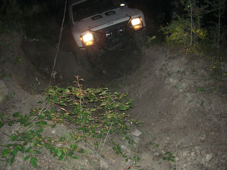 White Jeep Cherokee XJ going down a steep dirt hill at night