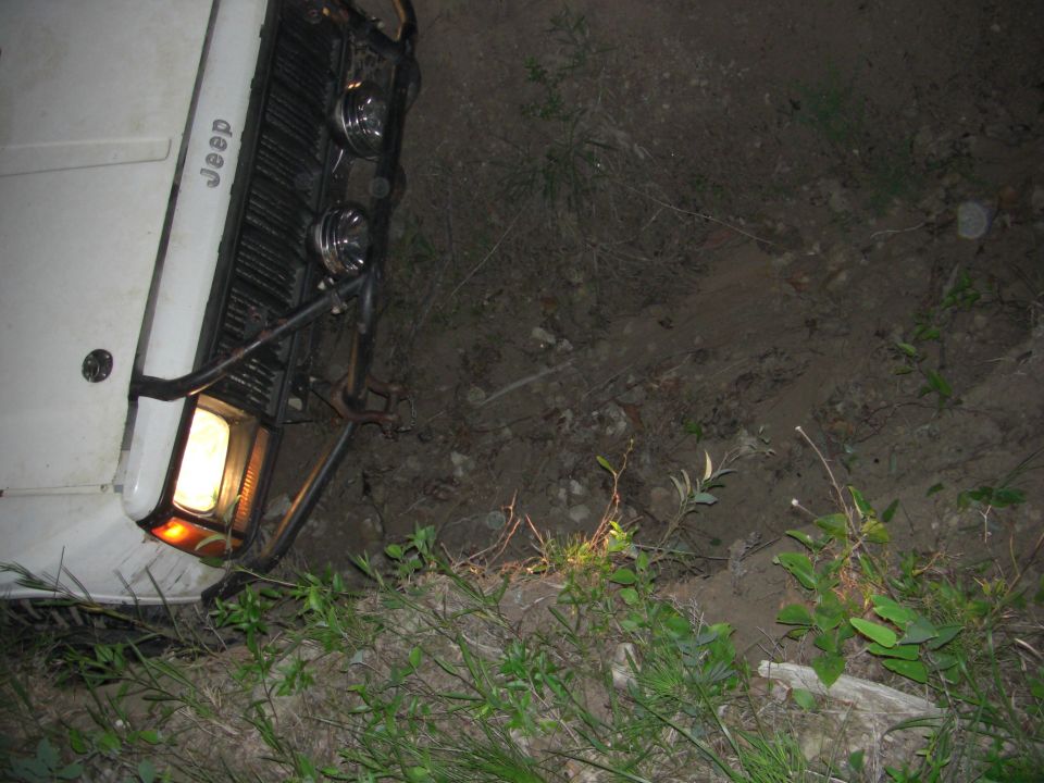 White Jeep with a black grille and chrome bumper, tilted on its side in dirt and grass
