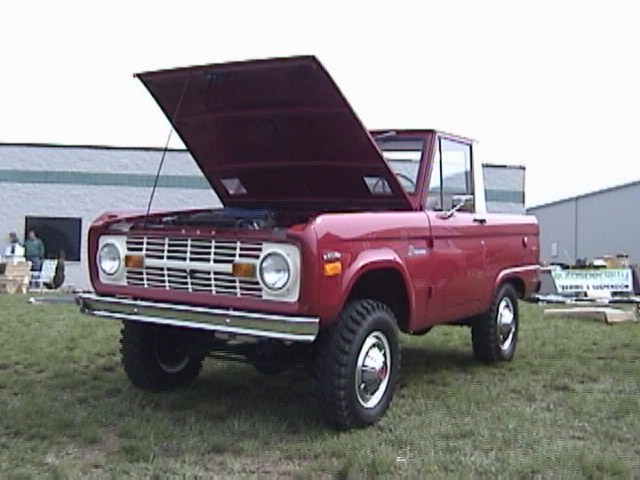 Red Ford Bronco, hood open, parked on grass in front of a building