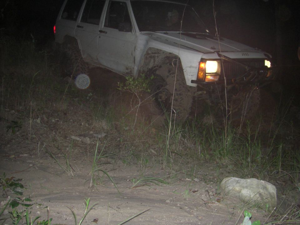 White SUV stuck in mud, front-right tire deep in dirt
