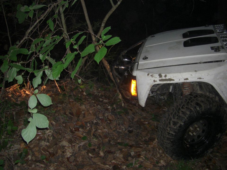 White SUV with off-road tires on a dirt path, front fender and headlight visible