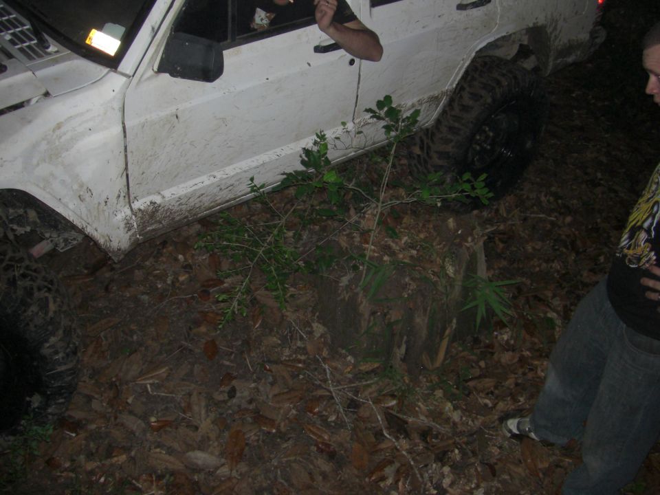 Side view of white off-road vehicle stuck in mud with people nearby