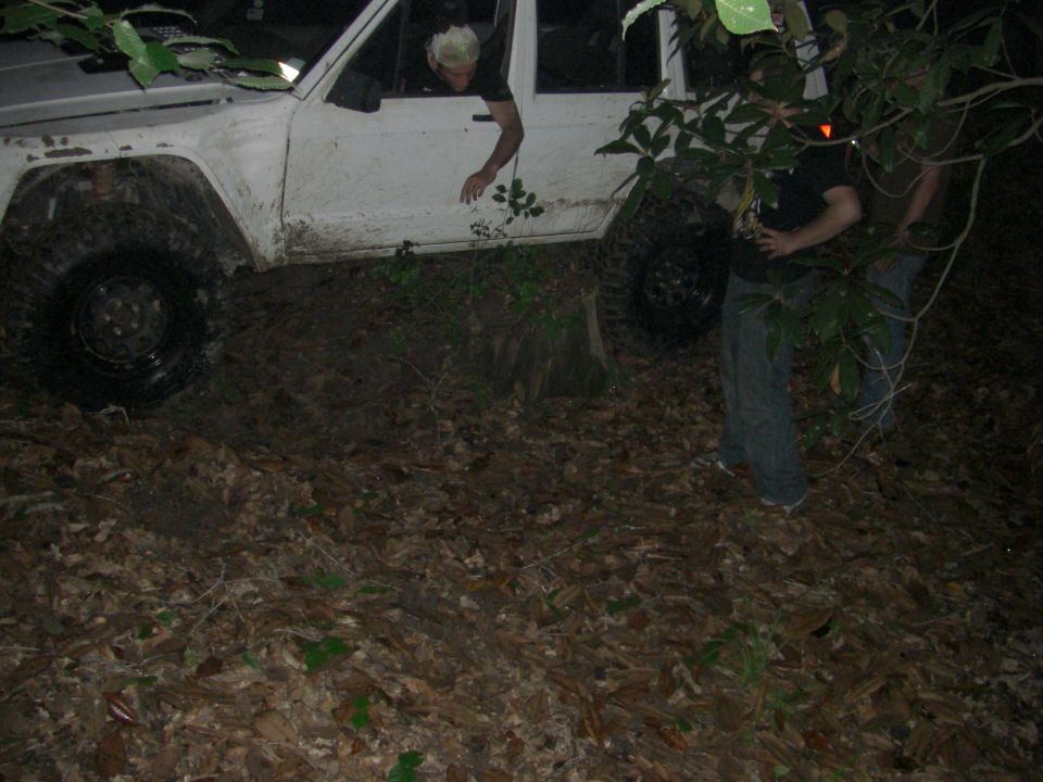 White SUV stuck in mud with people trying to get it out