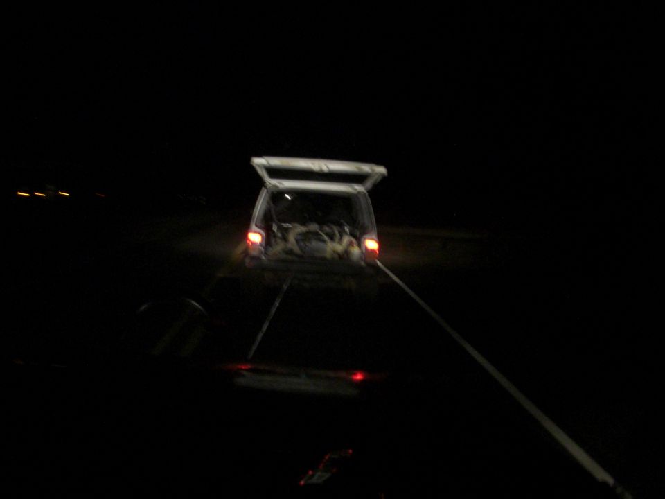 SUV with open tailgate being towed at night, tow strap visible