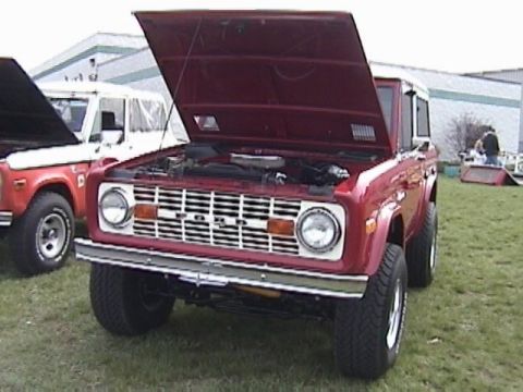 1995 Ford Bronco - Two Ford Broncos are parked outside with their hoods open, one red and one white.