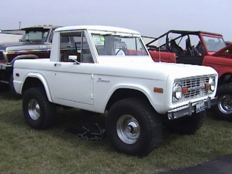 1995 Ford Bronco - A white first-generation Ford Bronco is parked on grass next to other vehicles.