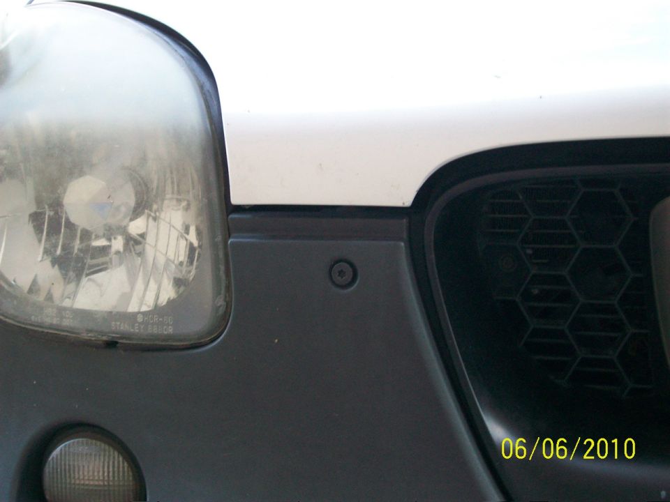 Close-up of white vehicle's front headlight, gray bumper and black honeycomb grille