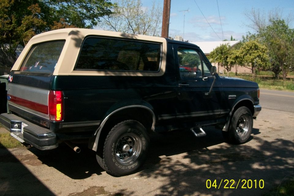 Dark green 1991 Ford Bronco with a tan top, parked on a street
