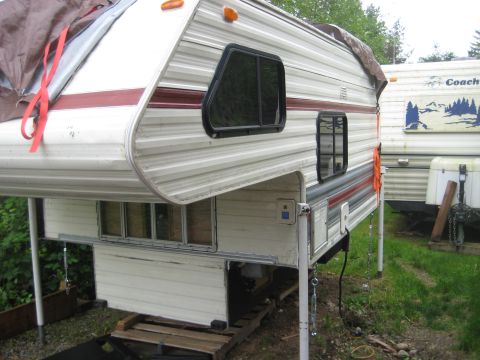 1978 Ford Bronco - A camper unit is shown supported by jacks, with a tarp covering part of its roof and another RV visible behind it.