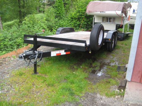 1978 Ford Bronco - Car hauler trailer with spare tire and a camper on top, parked on grass.