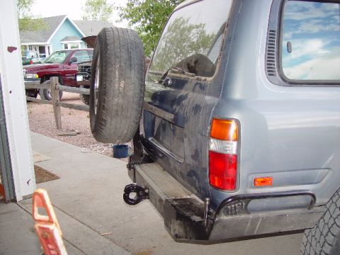 1993 Ford Bronco - Gray SUV's rear with spare tire; red pickup truck visible behind fence.