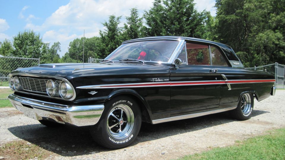 Black 1964 Ford Fairlane 500 with red stripe on side, parked outside