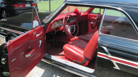 1992 Ford Mustang - The interior of a black 1964 Ford Fairlane features red vinyl seats and door panels, with a classic steering wheel and dashboard visible.