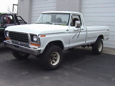 1995 Ford Bronco - A white pickup truck is parked in front of a garage door, with another vehicle partially visible to its left.