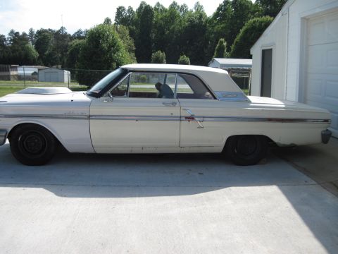 1992 Ford Mustang - A white 1964 Ford Fairlane is parked on a concrete driveway next to a white building.