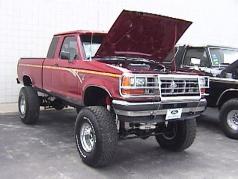 1995 Ford Bronco - This red Ford Ranger pickup truck, modified with a lift kit and large tires, has its hood open.
