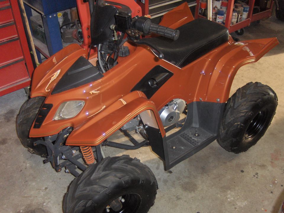 Orange ATV with black seat and handlebars, parked indoors