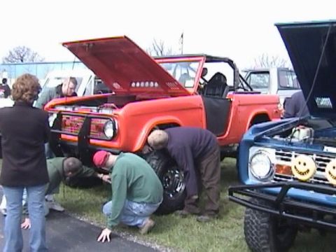 1995 Ford Bronco - Several people inspect the front wheel of an orange Bronco with its hood raised.