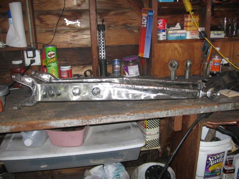 1989 Ford Bronco - Custom suspension control arm sits on a workbench in a cluttered garage setting.