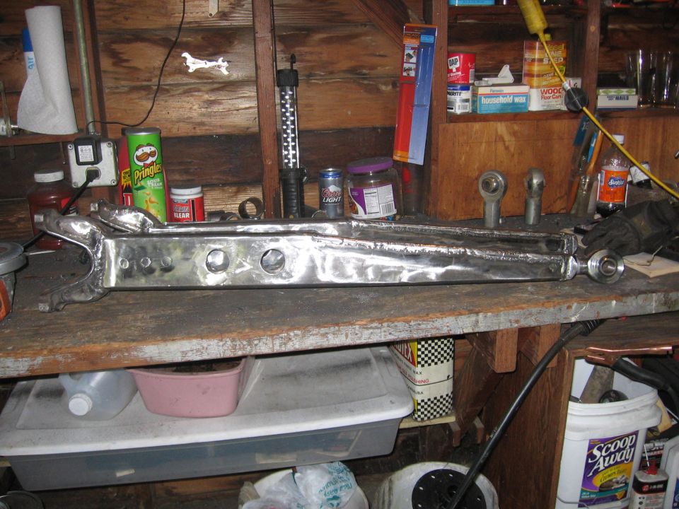 Modified suspension control arm on workbench with various workshop items in background